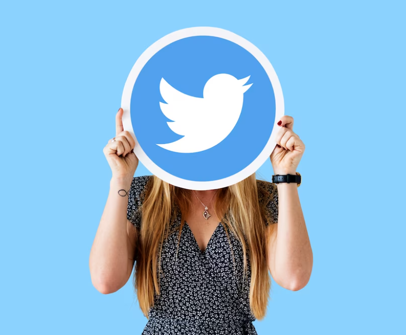 woman in black floral dress holding twitter logo on her face, blue wall behind her