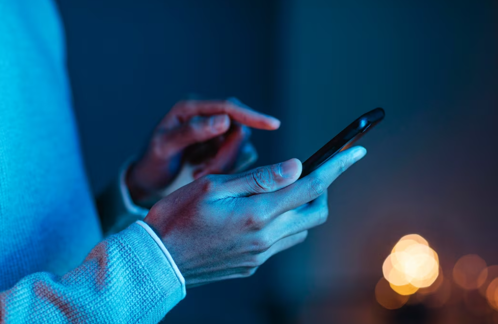 person holds a phone with one hand, and types with another  under a blue neon light
